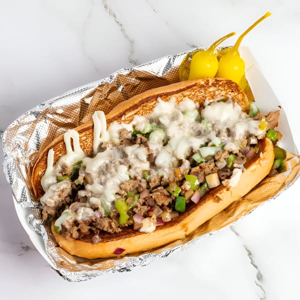 Cali Style Burger's cheesesteak sandwich with meat, peppers, onions, and melted cheese, served with two yellow peppers.