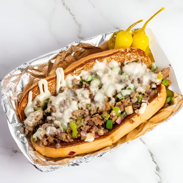Cali Style Burger's cheesesteak sandwich with meat, melted cheese, peppers, and onions, served with two yellow peppers.